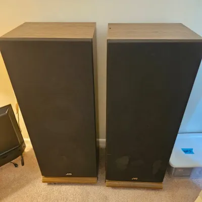 Pair of vintage JVC floor-standing speakers with wood grain cabinets and black fabric grilles.