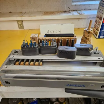 A keda DC dovetail jig system with various router bits, guide fingers, and accessories on a workshop bench.