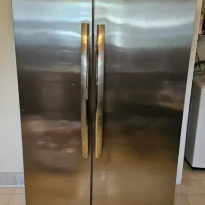 Frigidaire Gallery side-by-side refrigerator in a brushed stainless steel finish, showing some light surface wear.