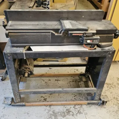 Vintage Craftsman jointer planer mounted on a black metal stand with a bottom shelf, showing signs of workshop use and sawdust.