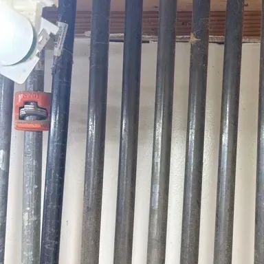 Collection of heavy-duty pipe clamps with red fixtures, organized on a wall-mounted wooden rack.