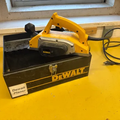 DeWalt corded hand planer resting on its original black metal carrying case, showing moderate signs of use.