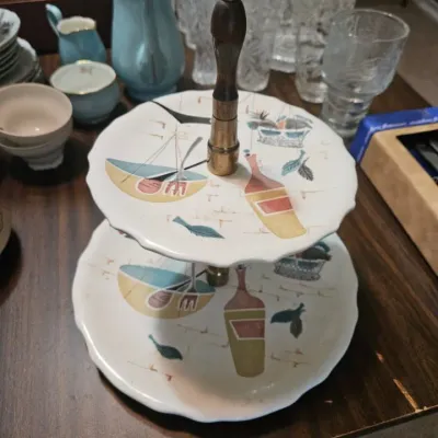 Vintage mid-century modern two-tier serving tray featuring a whimsical kitchen motif with bowls, bottles, and leaves, supported by a...