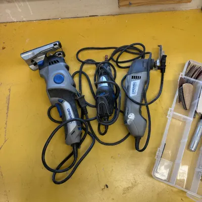 Three corded Dremel rotary and multi-max tools with a plastic organizer containing sanding accessories, showing moderate signs of use.