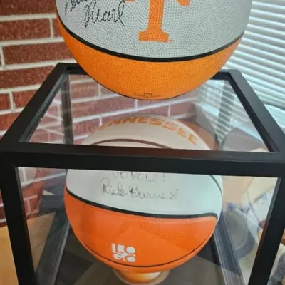 Two autographed Tennessee Volunteers basketballs, one signed by Bruce Pearl and resting on top of a black-framed glass display case...