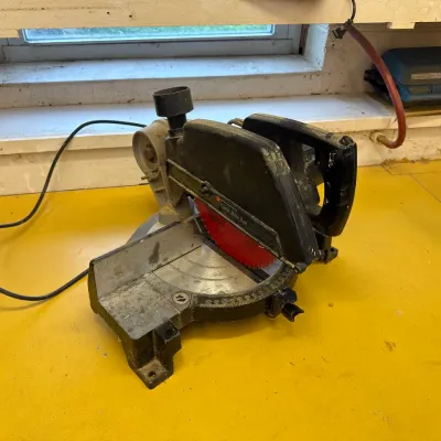 Vintage Black & Decker power miter saw with a red blade, showing signs of use and wear, resting on a yellow workbench.