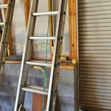 Aluminum extension ladder leaning against a wooden wall frame in a garage setting.
