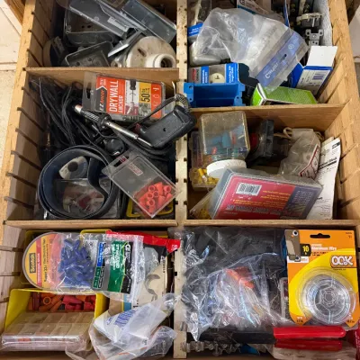 Wooden drawer organizer filled with various electrical and hardware supplies, including wire connectors, drywall anchors, electrical...