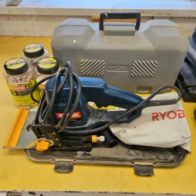 Ryobi corded biscuit joiner with its hard plastic carrying case, dust collection bag, and three jars of Ryobi wood biscuits.
