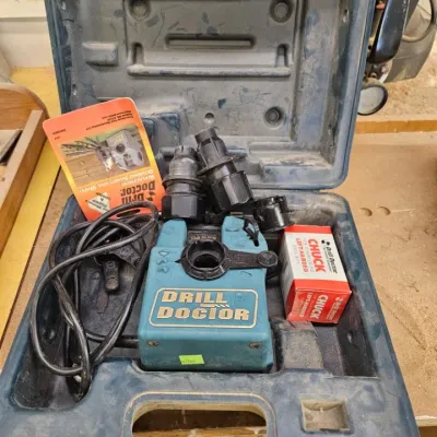 Drill Doctor drill bit sharpener with accessories, including chucks and manual, housed in its original blue plastic carrying case.