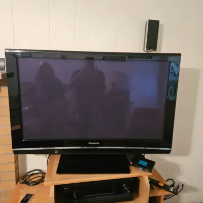 Panasonic Viera flat-screen television on a light wood media stand, shown with a Sony AV receiver and remote controls.