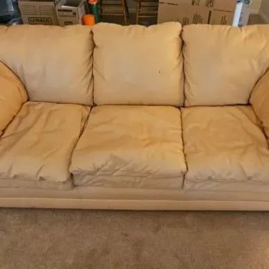 Plush three-cushion leather sofa in a light tan or beige color, showing some wear and creasing on the cushions.