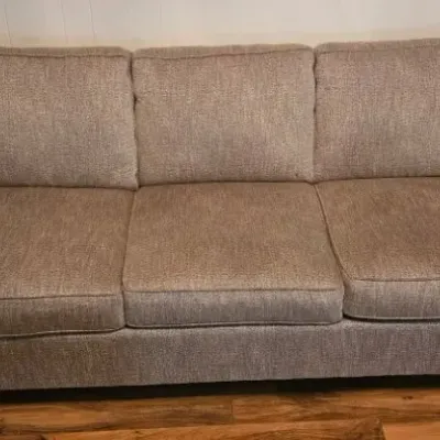 Three-cushion sofa upholstered in a textured beige fabric, featuring rolled arms and dark wood feet.