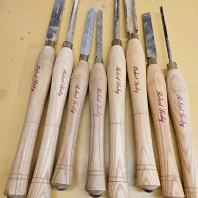Set of eight Robert Sorby woodturning chisels and gouges with light-colored wooden handles, showing some signs of use on the metal tips.