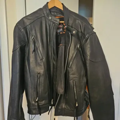 Milwaukee Leather black motorcycle jacket with multiple zippered pockets and a snap-tab collar, hanging on a wooden hanger.