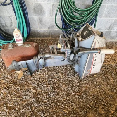 Vintage Evinrude outboard boat motor, showing signs of wear and age, accompanied by a metal fuel tank and a bottle of two-cycle engine oil.