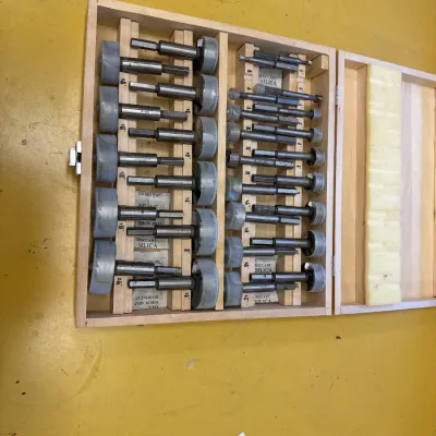 Multi-piece Forstner drill bit set in a fitted wooden storage case, showing various sizes in clean, lightly used condition.