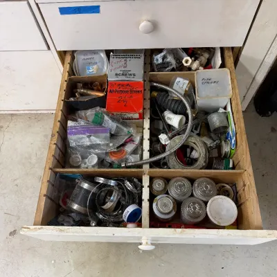 Assorted plumbing supplies, screws, hose clamps, and hardware organized in a divided wooden drawer.
