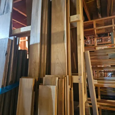 Assorted stacks of unfinished hardwood lumber and planks stored vertically in a workshop.