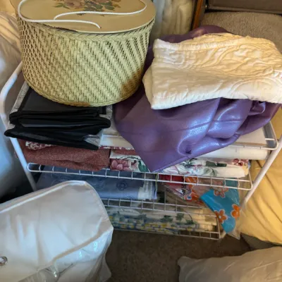 Sale Photo Thumbnail #189: Vintage woven sewing basket with a floral lid, displayed alongside various linens, fabrics, and bedding on a wire storage rack.
