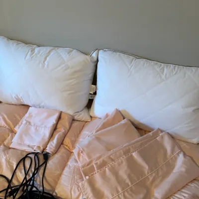 Sale Photo Thumbnail #167: Pair of white quilted bed pillows shown with folded light pink bed sheets and pillowcases.