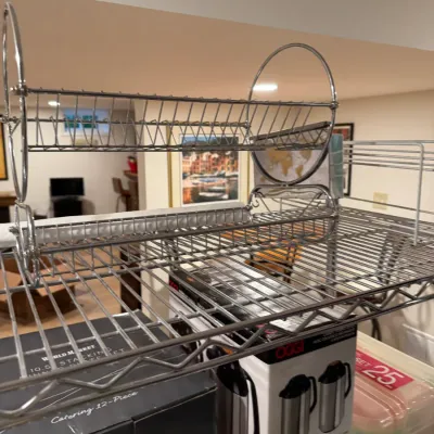Two-tier chrome wire dish drying rack sitting on a wire shelving unit alongside boxed kitchenware.