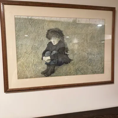 Andrew Wyeth framed art print depicting a young boy in a coonskin cap sitting in a grassy field, presented in a wooden frame with a wide...