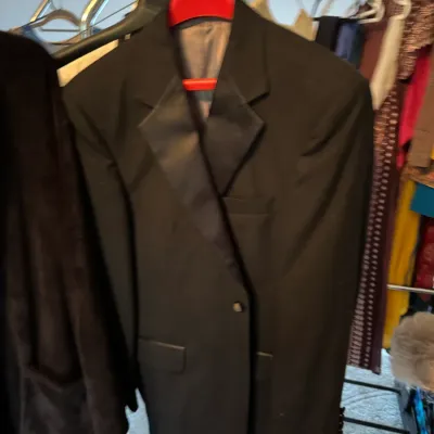 Classic black tuxedo jacket with satin peak lapels, hanging on a clothing rack.