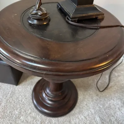 Traditional round wooden pedestal side table with a dark finish and an inset leather top featuring embossed detailing.