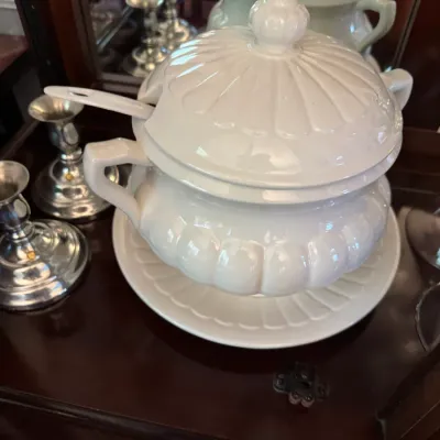 Sale Photo Thumbnail #249: White ceramic soup tureen with matching lid, underplate, and ladle, featuring a classic ribbed design, displayed alongside silver-plated candlesticks.