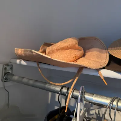 Sale Photo Thumbnail #172: Light orange woven sun hat with an adjustable chin strap, resting on a closet shelf.