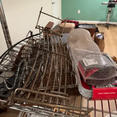 Sale Photo Thumbnail #103: Assorted grilling accessories including metal cooking grates, a grill scrubber, and Weber aluminum drip pans on a wire shelf.