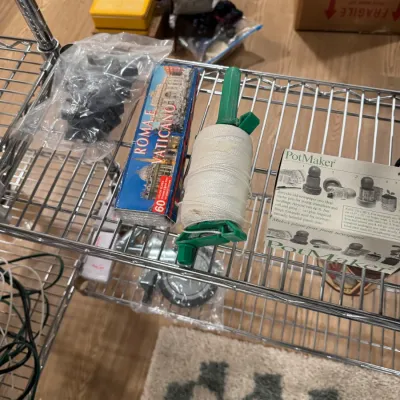 Sale Photo Thumbnail #119: Assorted household items on a wire shelf, including a box of Rome and Vatican color slides, a green plastic string reel, and a PotMaker kit.