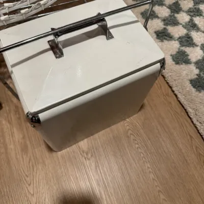 Vintage white metal cooler with a chrome locking handle and reinforced corners, showing minor surface wear.
