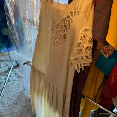 Vintage cream-colored dress featuring intricate lace cutouts on the neckline and short sleeves, with a pleated skirt, hanging on a...
