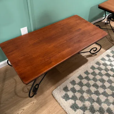 Rectangular wooden coffee table with a warm reddish-brown finish, supported by a black wrought iron base featuring scrollwork details.