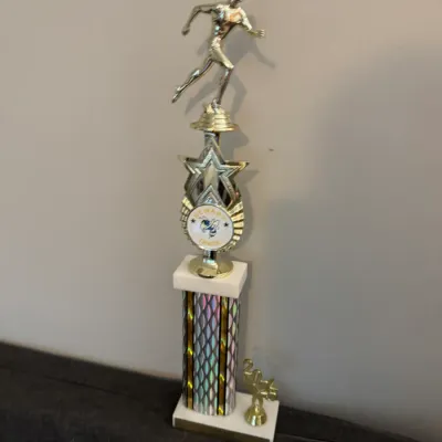 Sale Photo Thumbnail #129: Vintage Newark Track trophy featuring a golden runner figurine atop a star emblem and a patterned column, dated 2015.