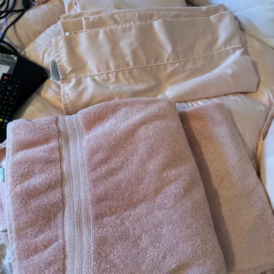 Sale Photo Thumbnail #163: Assorted pink linens, including folded bath towels with woven borders and matching bed sheets.