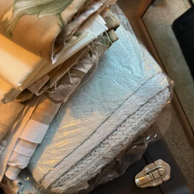 Sale Photo Thumbnail #137: Stack of vintage linens and textiles, including floral patterned fabrics and a light blue textured blanket sealed in plastic.