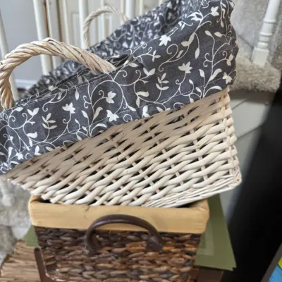 Sale Photo Thumbnail #268: Two woven storage baskets, including a white wicker stair basket with a grey floral fabric liner and a dark brown rectangular basket with a tan liner and handles.
