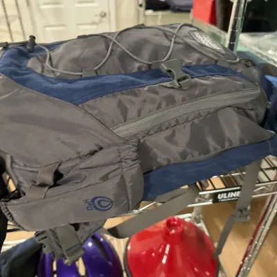 Grey and blue High Sierra hydration backpack resting on a wire shelf, showing light wear.
