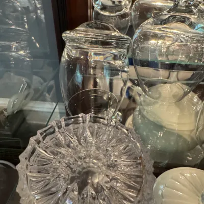 Sale Photo Thumbnail #253: Assorted clear glassware, including a cut crystal bowl and lidded glass jars, displayed on a glass shelf.