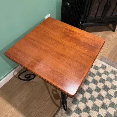 Square wooden end table with a warm reddish-brown finish and decorative black wrought iron scroll legs.