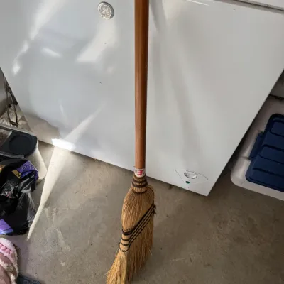Sale Photo Thumbnail #217: Vintage straw broom with a wooden handle, shown leaning against a white GE chest freezer.