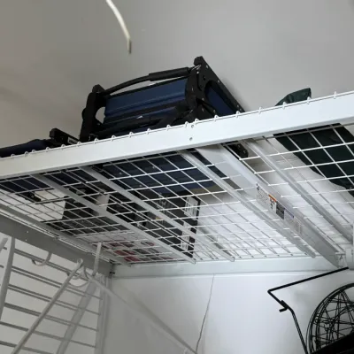 Sale Photo Thumbnail #206: White wire overhead garage storage rack holding a folded blue camping chair and other items.