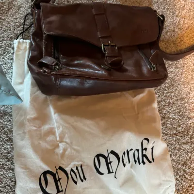 Mou Meraki brown leather messenger bag with adjustable shoulder strap, buckle closure, and zippered pockets, accompanied by its original...