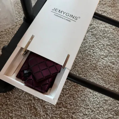 Sale Photo Thumbnail #156: Jemygins necktie and pocket square set in burgundy with a geometric grid pattern, presented in its original white box with a silver-tone tie clip.