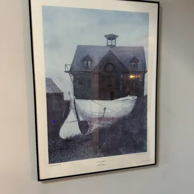 Sale Photo Thumbnail #262: Framed exhibition poster of Andrew Wyeth's "Liberty Launch," featuring a white dory in front of a coastal house, presented in a simple black metal frame.