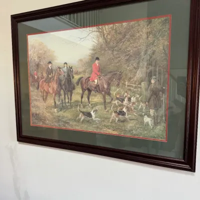 Framed print depicting a traditional English fox hunt scene with riders on horseback and hounds, presented in a dark wood frame with...