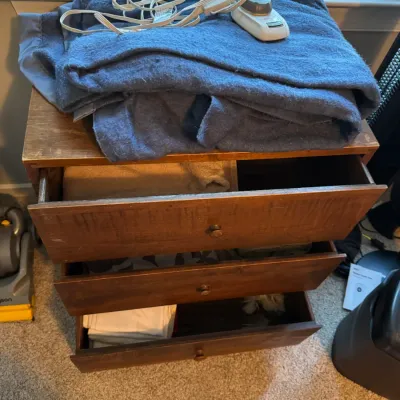 Sale Photo Thumbnail #142: Vintage three-drawer wooden chest with simple round knobs, showing some surface wear, topped with a folded blue electric blanket.